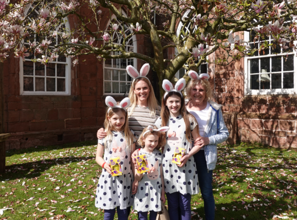 Mother, grandma and three girls wearing bunny ears and holding Easter eggs outside in Spring