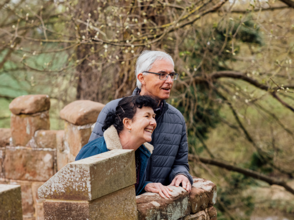 Middle-aged male and female couple smiling and looking out over the Castle grounds, leaning over a crenellated wall
