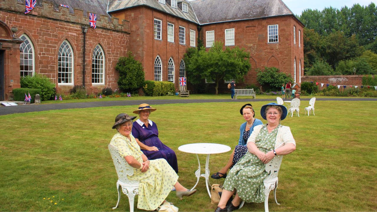 Four ladies sitting outside and dressed in 1940s fashion in the Hartlebury Castle grounds