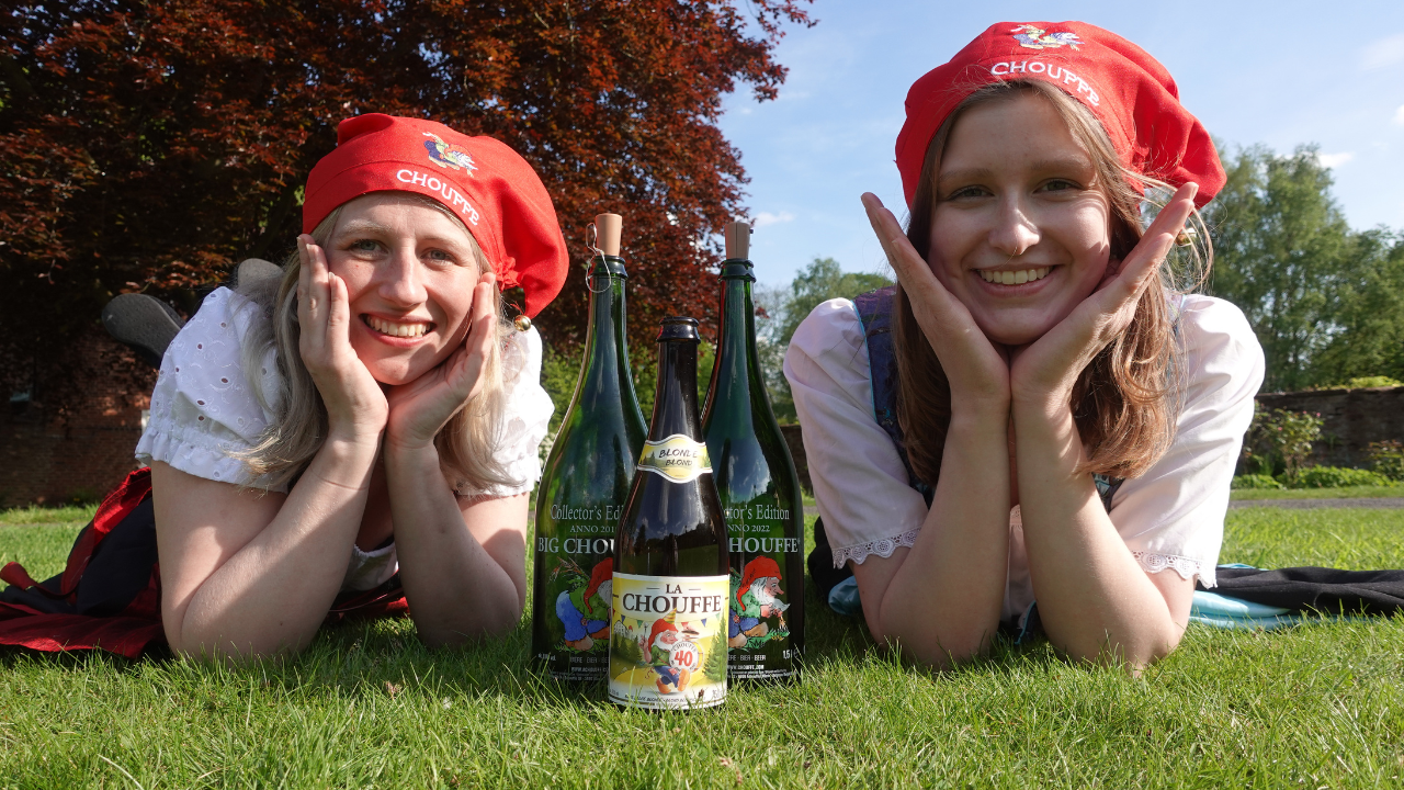 Two women outdoors and dressed as gnomes, wearing Chouffe hats with Chouffe beer bottles by them