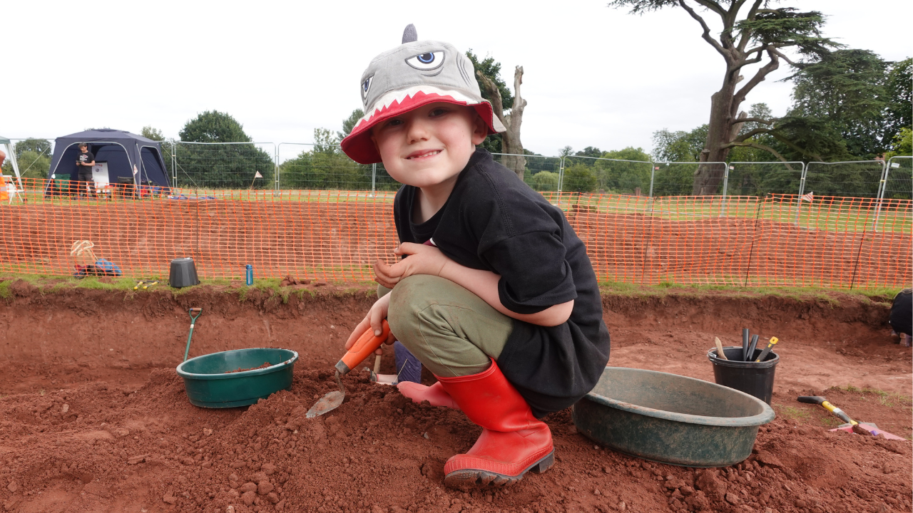 Young boy on an archaeological dig site, crouching with a trowel in his hand