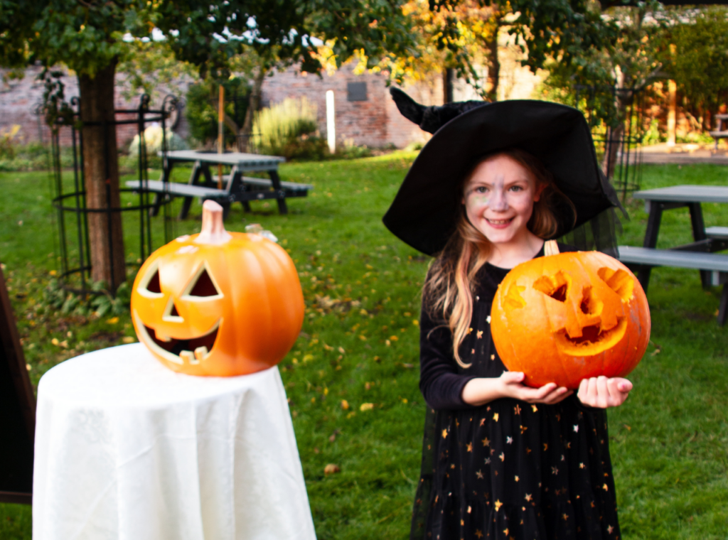 Girl in a witch costume holding a carved pumpkin outdoors