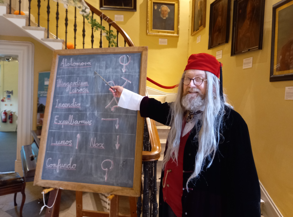 Professor Bumbledum points to a list of spells on a blackboard in the Hartlebury Castle Great Hall