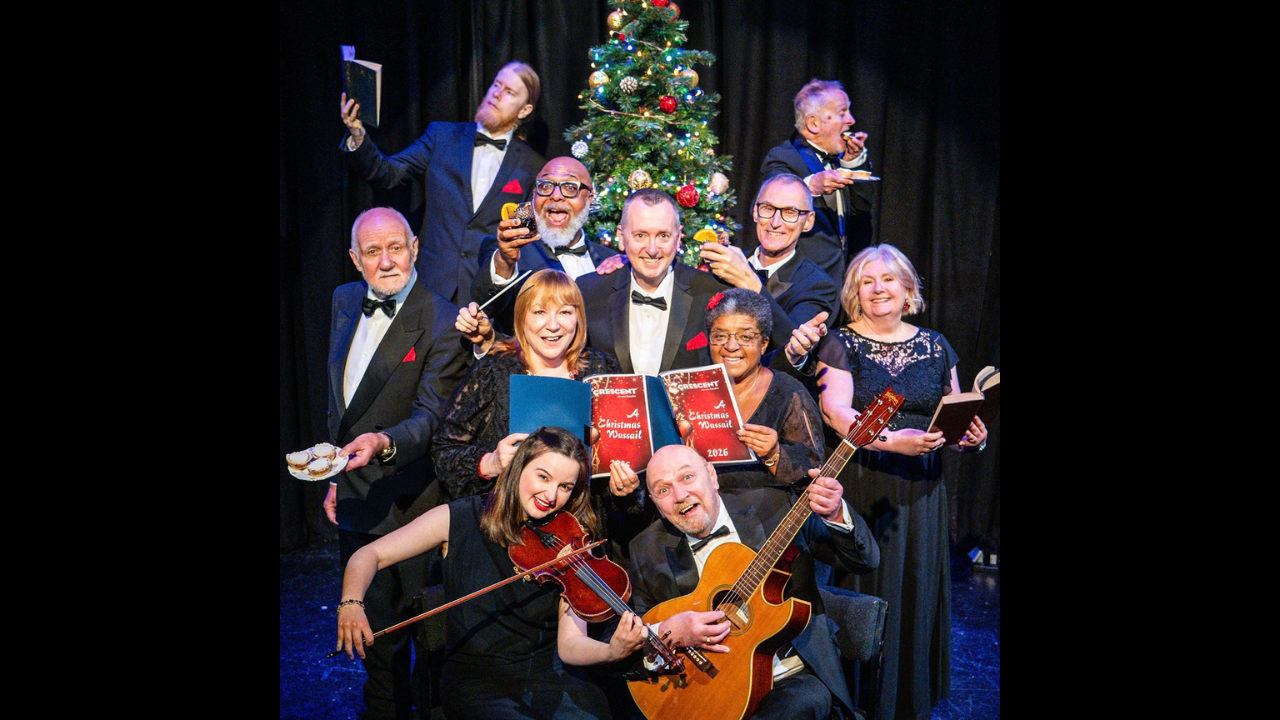 Group of performers and musicians dressed in formal black, posing in front of a Christmas tree