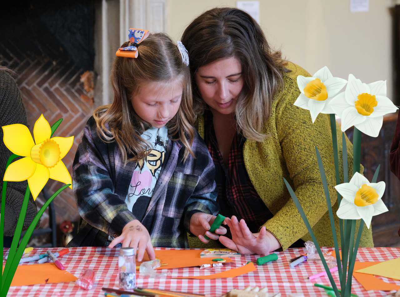 A woman and a girl make paper crafts on a banner featuring daffodils