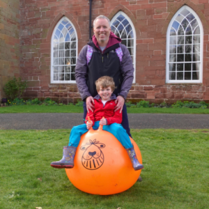 Man balancing a boy sitting on a space hopper outside Hartlebury Castle