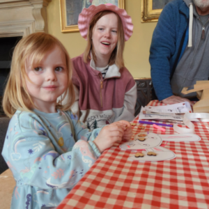 Woman smiling at a girl doing bunny mask crafts