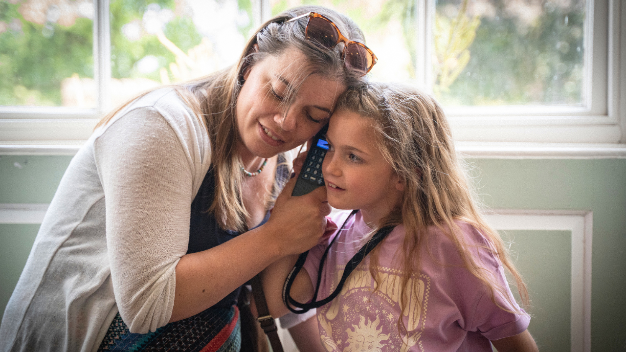 Woman and girl listen to an audio guide from a window seat indoors