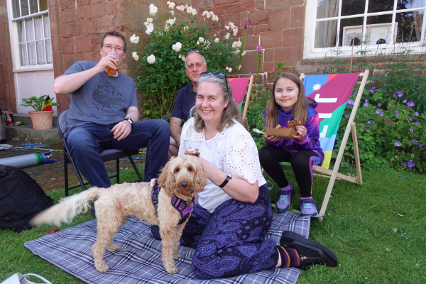 A family and a dog relaxing on deck chairs and a picnic blanket