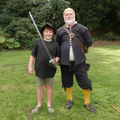 Boy wears a helmet and holds a sword while posing for a photo with a Civil War re-enactor