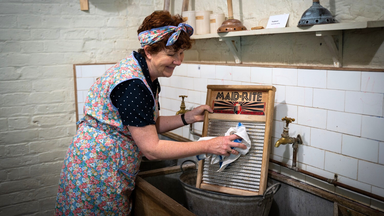 Woman scrubs on a washboard while wearing old fashioned clothes