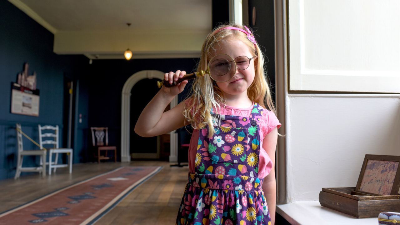 Girl looks through magnifying glass in long corridor