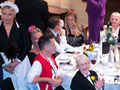 A seated audience laughing next to an actor dressed as a maid