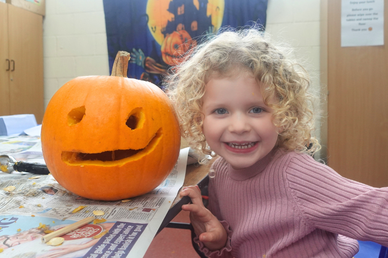 Smiling girl posing next to a carved pumpkin with a Halloween banner in the background