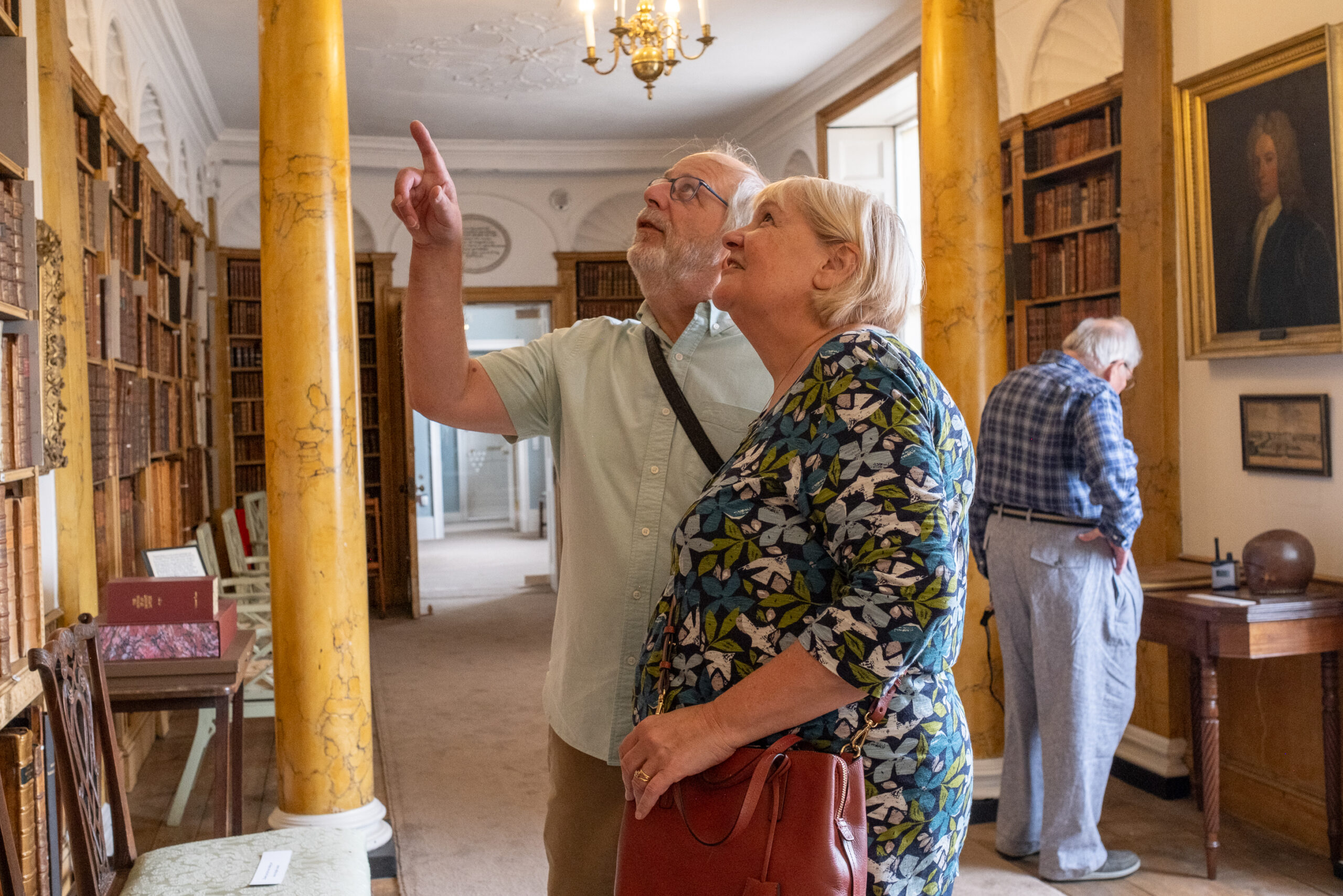 A older man and woman point and look curiously up into the bookshelves in the long corridor of the Castle's Hurd Library