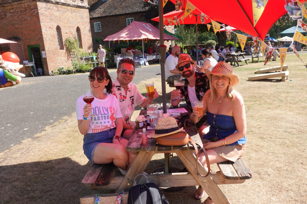 Two men and two women at a Castle picnic bench, posing for the camera with beer