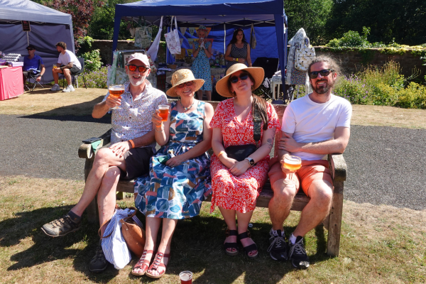 Two men and two women sitting on a bench, smiling and holding beer