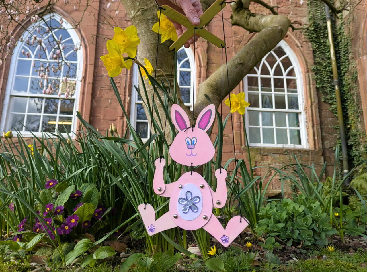 Wooden bunny maisonette puppet held up outdoors by a tree and daffodils