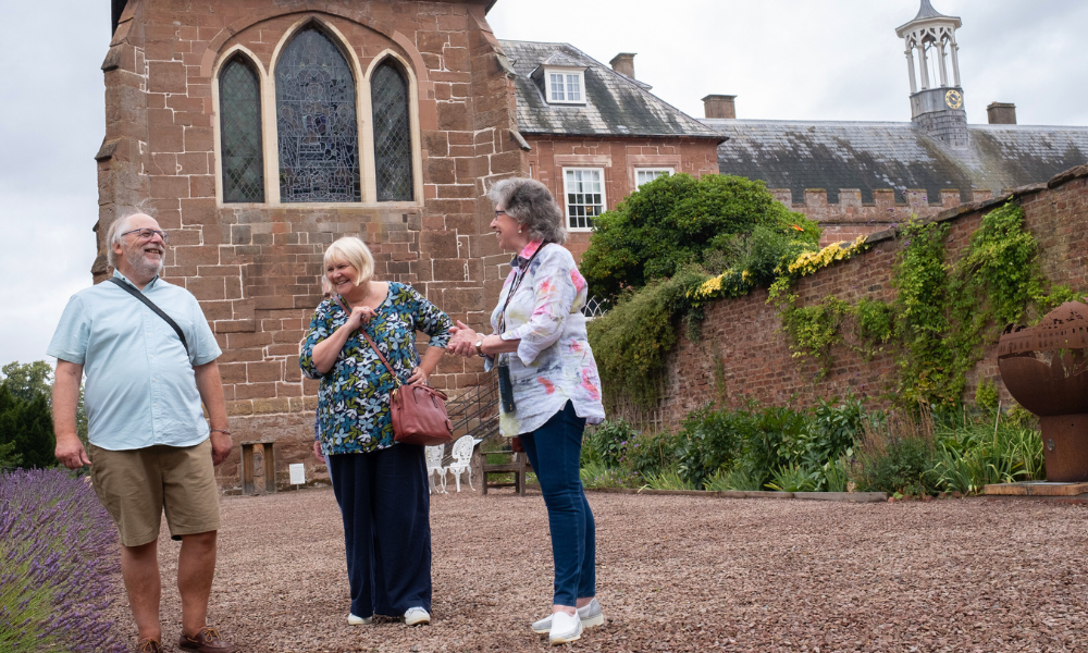 An older man and two older women smile outside Hartlebury Castle on the terrace of the Queen Elizabeth Walk