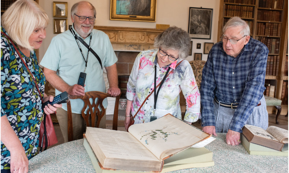 Two older women and two older men looking at a large book in the Hurd Library