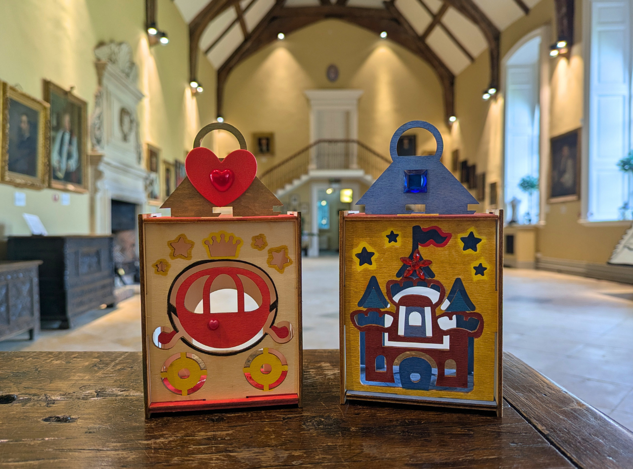 Two decorated wooden lanterns with carriage and Castle designs in Hartlebury Castle's Great Hall