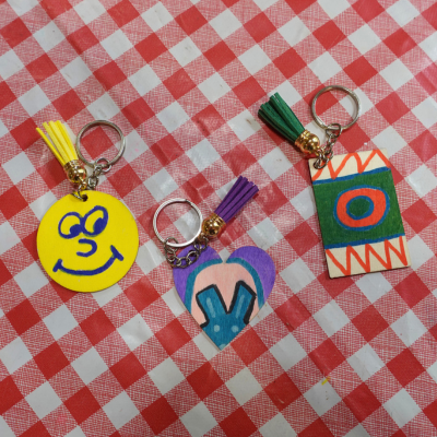 Three wooden keyrings on a paisley background - decorated with a smiley face, rabbit ears, and a circle and zigzags