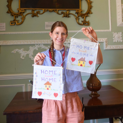 Young woman holding up two material banners reading 'Home sweet home' with houses and hearts.