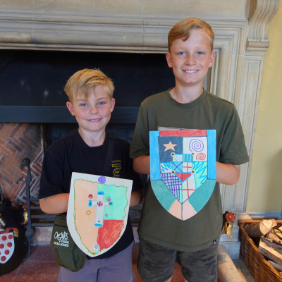 Two young boys holding colourful wooden shields featuring their own coats of arms