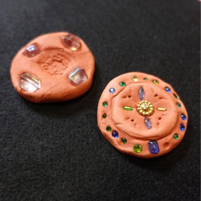 Two clay coins featuring gems and stamped designs