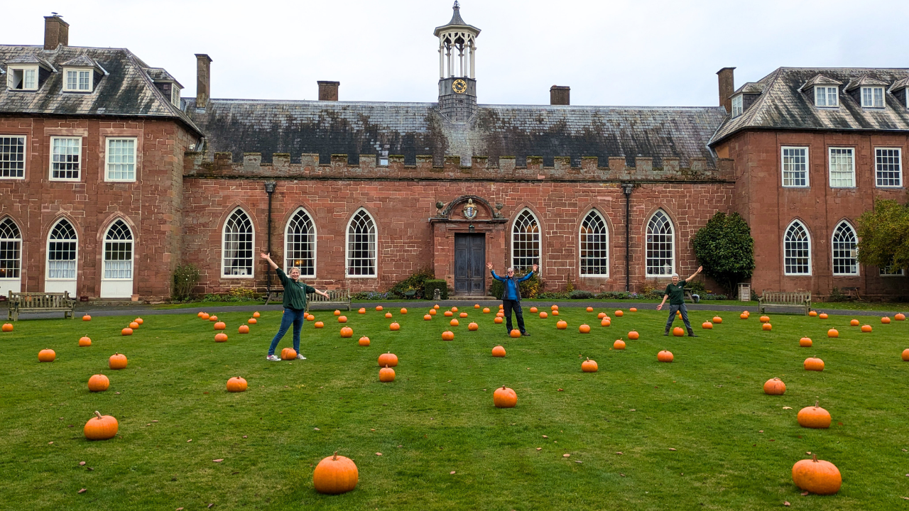 Three woman with arms raised in celebration on the Castle's Carriage Circle Pumpkin Patch, with the Castle behind them