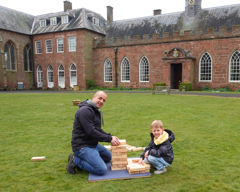 Man and boy play Jenga on the Carriage Circle in front of Hartlebury Castle