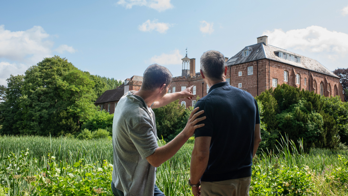 Two men look across a green-reeded moat to Hartlebury Castle, with one pointing there